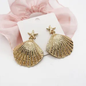 Detail view of textured gold starfish and sea shell drop earrings