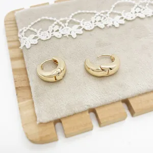Close-up of chunky gold-plated hoop earrings on a grey velvet display