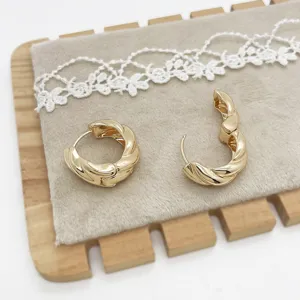 Macro view of minimalist gold-tone twisted chunky hoop earrings on velvet padding