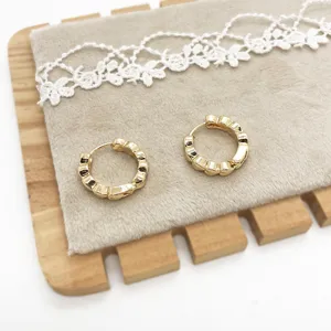 Detailed macro view of gold-tone wavy geometric hoop earrings on a soft grey display pad