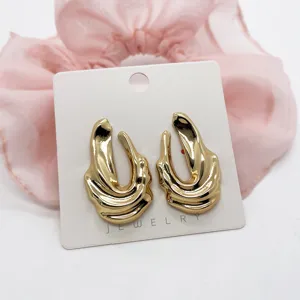 Detail view of chunky gold geometric earrings with a glossy ocean wave texture finish