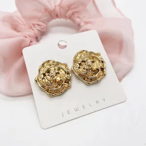 Macro view of golden rose-shaped stud earrings on a jewelry card with pink backdrop