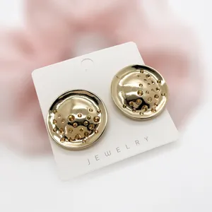 Detailed view of golden textured geometric stud earrings on white jewelry card