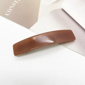 Vue détaillée d'une barrette rectangulaire en acétate marron brillant sur fond minimaliste