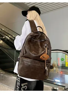 Detailed shot of a vintage brown soft leather backpack with a cute teddy bear pendant.