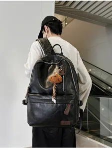 Detail view of a vintage black soft leather backpack on model with plush bear accessory