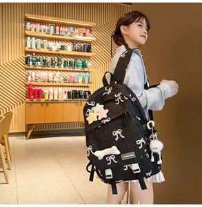 Detalle de una linda mochila acolchada negra con bordado de lazos y colgante de peluche