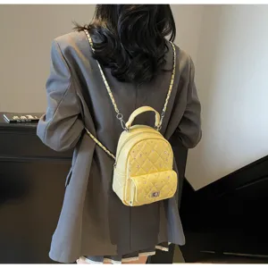 Back view of model wearing a mini yellow quilted backpack with chain straps and crystals