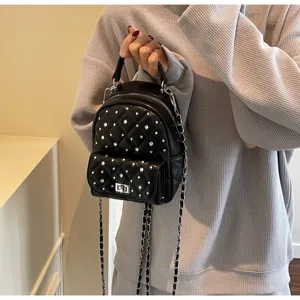 Detail view of a black quilted mini backpack featuring rhinestone pearls and silver chain strap