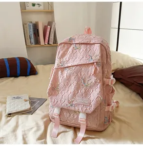 Detalle de la mochila escolar acolchada rosa con bordados de lazos de colores en la cama