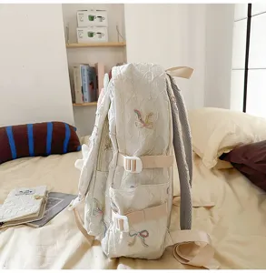 Vista lateral de mochila escolar blanca con bordado de lazos coloridos y hebillas