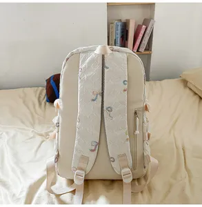 Vista detallada de las correas y el bordado de lazo acolchado en esta mochila escolar crema.