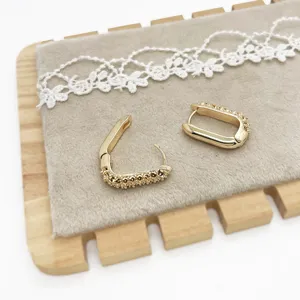 Detail shot of gold geometric hoop earrings with textured surface on grey velvet