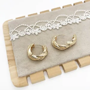 Close-up detail of gold-plated twisted hoop earrings on a luxury velvet display stand.