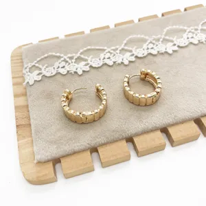 Macro view of gold-colored geometric textured hoop earrings in a minimalist style