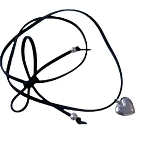 Détail d'un collier choker en cuir noir avec un pendentif cœur argenté et un nœud papillon