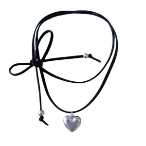 Détail du pendentif en forme de cœur argenté et du nœud en cordon de cuir noir du collier.