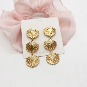 Detailed macro shot of golden triple-tier sea shell earrings with vintage metallic texture.