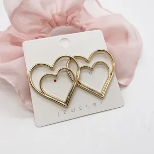 Detailed shot of elegant gold-toned double heart stud earrings on display card.