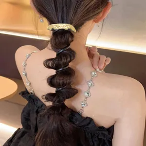 Detailed view of a golden metallic clip and black spiral hair tie on a stylish bubble braid.
