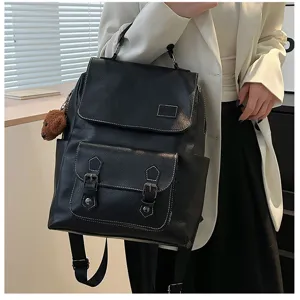 Dettaglio di uno zaino vintage in pelle PU nera con doppia fibbia e ciondolo a forma di orso.