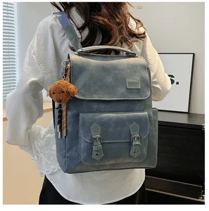 Vista posteriore di una donna con uno zaino vintage in pelle PU blu e ciondolo a orsetto.