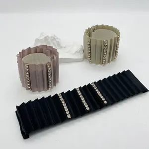 Detalle de pinzas para el cabello de tela plisada con filas de pedrería en tres colores