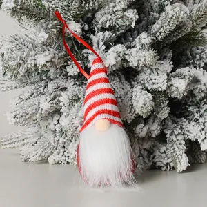 Detail shot of a cute red and white knit Christmas gnome ornament hanging on a snowy tree branch.