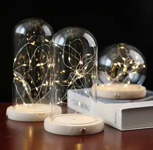 Détail charmant de cloche en verre avec guirlande lumineuse LED chaude sur base en bois.