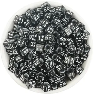 Macro detail of 6mm black square acrylic beads with funny emoji faces in a white bowl
