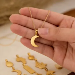 Detailed view of a gold-plated stainless steel crescent moon pendant held by a hand