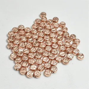 Primer plano macro de cuentas redondas de acrílico oro rosa de 7 mm con letras grabadas