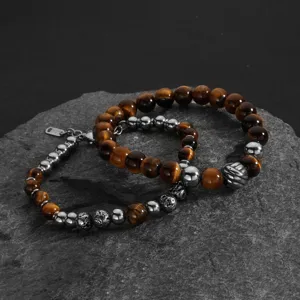 Nahaufnahme von Armbändern aus Tigerauge und Lavastein auf einer dunklen Felsfläche.