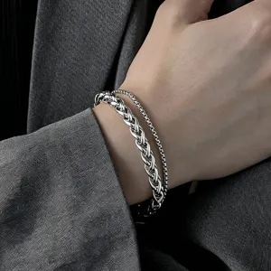Macro view of double-layer stainless steel silver Cuban chain bracelet on men's wrist.