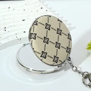 Macro detail of a round foldable makeup mirror keychain featuring a beige floral leather cover