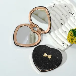 Close-up detail of black glitter heart-shaped folding compact mirror with gold bow accent
