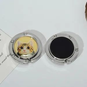 Detail showing both sides of a foldable metal purse hook with cute cat print and rubber base