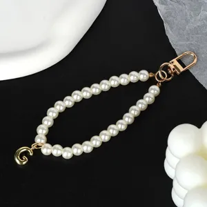 Detail of elegant white pearl keychain with gold initial G charm on black background