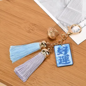 Detail view of a tassel keychain featuring a lucky charm tag and golden bell.