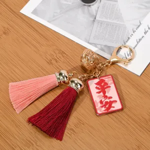 Close-up of the red blessing tag and dual-color tassels on this golden bell keychain