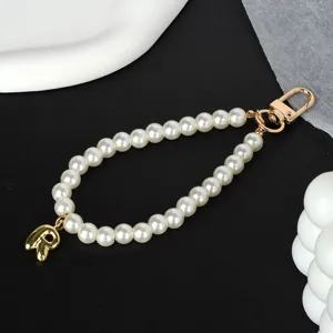 Close-up detail of an elegant white pearl phone chain with a gold metal letter R charm