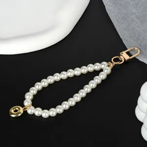 Detail view of an elegant pearl keychain with a gold-toned clasp on black background