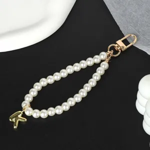 Close-up of elegant white pearl phone strap with a gold letter K charm and metal clasp