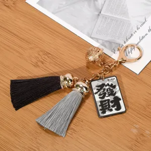 Detail view of a golden keychain with tassels and a 'RICH' charm displayed on a wooden surface.