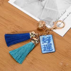 Detailed view of golden bell keychain featuring blue tassels and a Good Luck charm