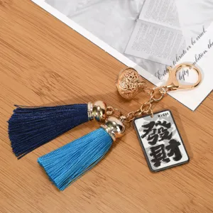 Close-up detail of a blue tassel keychain featuring a golden hollow bell and Rich tag