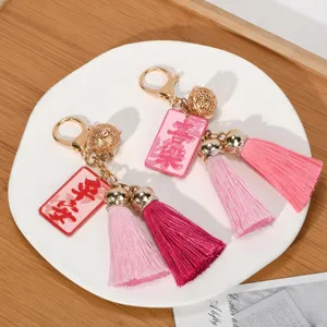 Close-up of blessing tassel keychains with golden bells and pink tassels on a white plate.