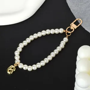 Macro view of white pearl phone strap with a golden letter B charm and metal clasp.