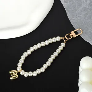 Detail view of a white pearl phone strap with a golden number three pendant ornament.