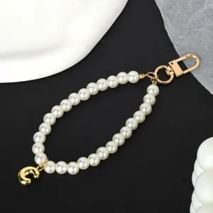 Close-up detail of a white pearl phone chain featuring a shiny gold-plated letter C charm